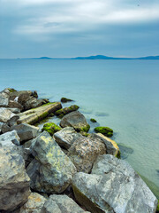 Calm waters and rocky shores create a serene coastal scene along the tranquil beach at sunset under a soft blue sky