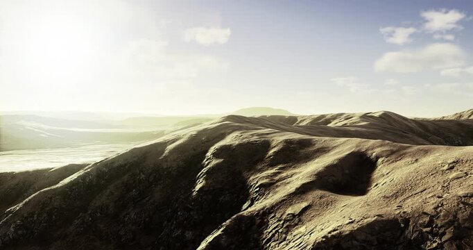 Gentle hills undulate beneath a warm sun, casting long shadows across rugged terrain. The serene landscape exudes tranquility, inviting exploration and adventure in natures embrace.