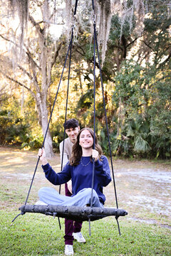 Young woman on a swing being pushed by smiling young man.