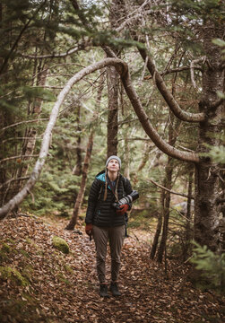 female hiker with camera framed by arch like tree branch, Maine