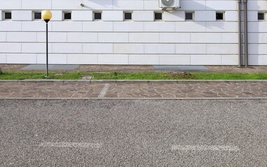 Elegant white stone tiled facade with small windows. Sidewalk, strip of grass and street in front. Background for copy space. 