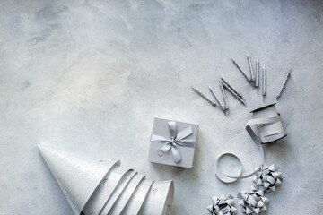 Festive party decoration in silver color with gift box and carnaval caps on gray stone background, top view
