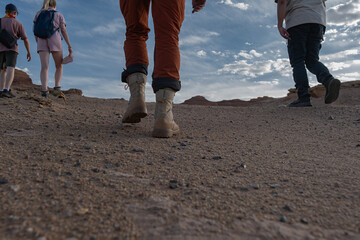 A group of travelers in bright clothing hikes up a rocky desert slope in Mongolia. Low-angle shot emphasizes their hiking boots against the clay hills and a vast blue sky. © ANDREY