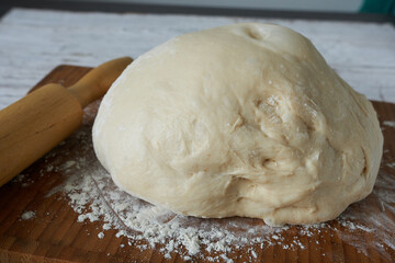 Bread dough and rolling pin on a wooden board with flour.