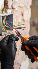 Professional electrician in black gloves using pliers to work with colorful electrical wires in wall junction box. Skilled tradesman performing electrical installation or repair work indoors.