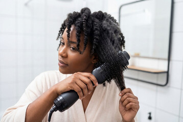 Young woman styling curly hair with hot air brush in bathroom, daily self care and home beauty routine for natural hair maintenance and personal grooming