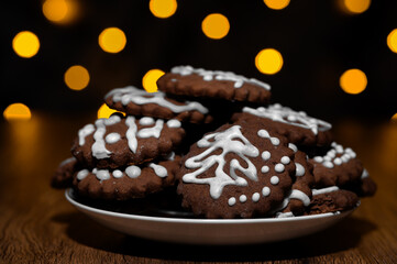 On the table lies a plate with baked, handmade gingerbread cookies with icing, a bokeh background made of Christmas lights