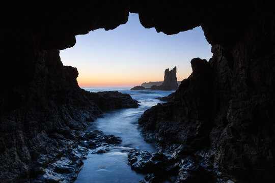 Looking out from the iconic cave at Cathedral Rocks located amongst the rocky coastline near Kiama on the South Coast of NSW, Australia. Captured with a long exposure on a clear sky on sunrise.