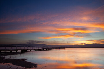 Boonerah Point jetty under a beautifully vibrant sky looking west to the mountains on Lake Illawarra, New South Wales, Australia.
