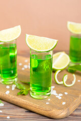Sweet refreshing mint liqueur, with ice and mint leaves on table background, Shots with lime slice and mint flat lay
