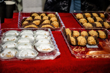 Traditional festive sweets displayed on red tablecloth in glass trays, powdered sugar cookies and nut pastries arranged for Christmas celebration, winter holiday dessert table at seasonal market