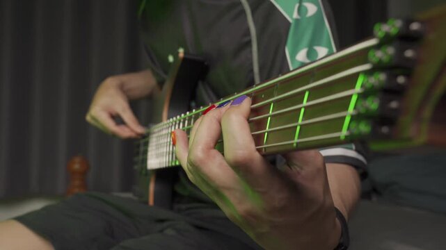 Close up of finger musician at the bass guitar , musician playing bass guitar in the room and with neon lights ,Bassist practicing in a bedroom studio.