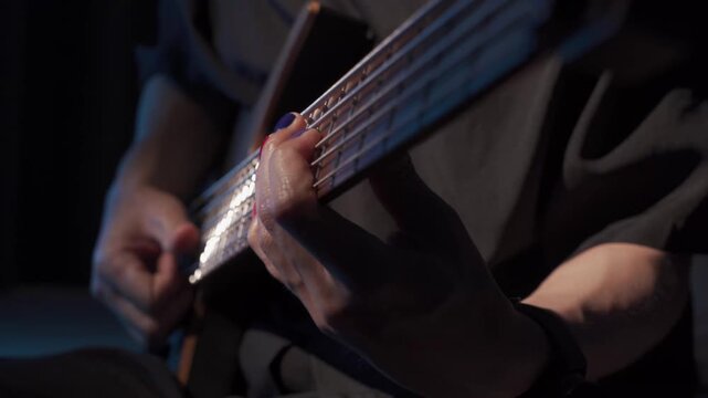 Close up of finger slap bass of musician at the bass guitar , musician playing bass guitar in the room and with neon lights ,Bassist practicing in a studio.