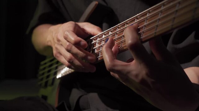 Close up of finger tapping bass of musician at the bass guitar , musician playing bass guitar in the room and with neon lights ,Bassist practicing in a studio.
