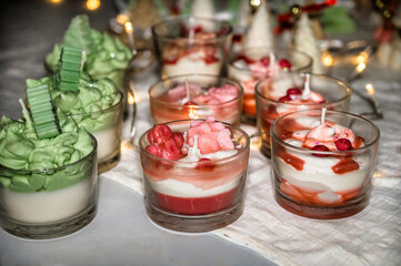 Decorative holiday candles in glass cups shaped like Christmas desserts, glowing warm lights on festive table, cozy winter atmosphere, seasonal decor concept for Christmas and New Year