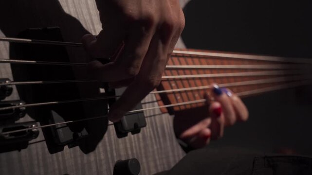 Close up of finger musician at the bass guitar , musician playing bass guitar in the room and with  spotlights ,Bassist practicing in a  studio.