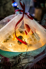 Festive illuminated decor wrapped in translucent fabric with red ribbon, soft warm glow creating cozy winter atmosphere, magical holiday lighting, handcrafted seasonal styling, intimate festive mood