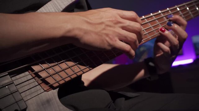 Close up of finger musician at the bass guitar , musician playing bass guitar in the room and with  spotlights and neon light ,Bassist practicing in a bedroom studio.
