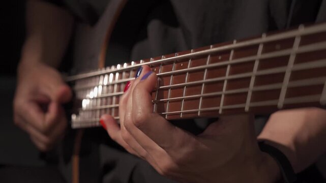 Close up of finger musician at the bass guitar , musician playing bass guitar in the room and with  spotlights ,Bassist practicing in a studio.
