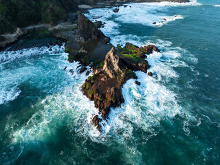 Aerial view of rugged cliffs meet the turquoise sea, waves crashing against the rocky shore at Pantai Watu Lumbung, Special Region of Yogyakarta, Indonesia.