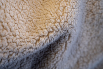 Macro of folded beige sherpa fleece fabric. The soft, warm, and cozy texture creates an abstract background with a shallow depth of field.