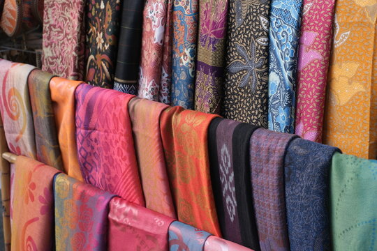Vibrant assortment of traditional Indonesian textiles, including batik and woven fabrics, hanging in a market stall. Popular for clothing and cultural crafts.