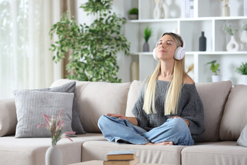 Blonde woman wearing headphone meditating at home