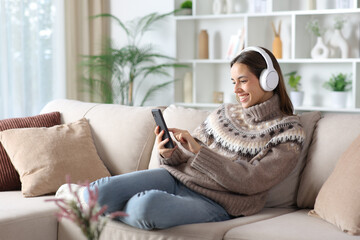 Happy woman listening audio in winter using phone