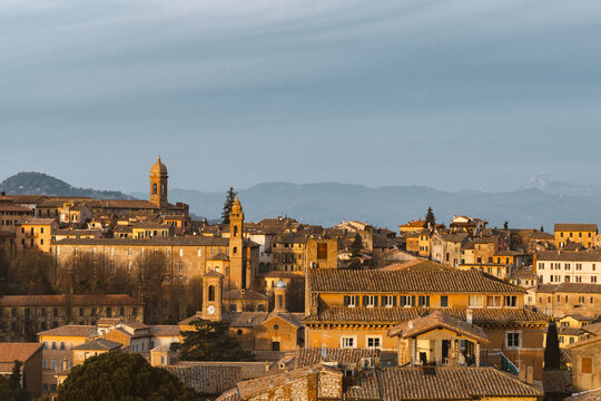 Aerial view of golden sunlight bathing the terracotta rooftops and ancient bell towers of the medieval town, Morcella, Umbria, Italy.