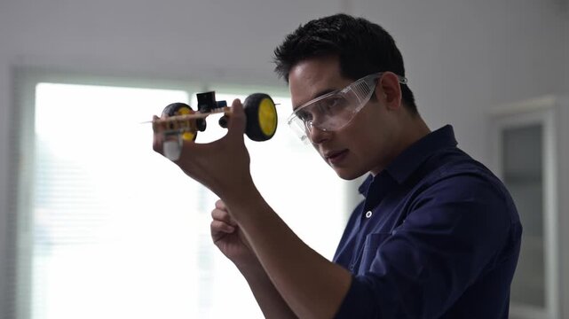 A man wearing a blue shirt and goggles is holding a yellow object. He is looking at it