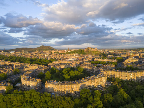 Aerial view of the crescent-shaped Georgian architecture of Moray Feu, bathed in golden light, with Edinburgh Castle perched atop a distant crag, Moray Feu, Scotland, United Kingdom.