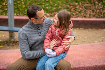 Fototapeta premium Father and daughter sitting close and talking on the playground border. Tender moment of connection and support.
