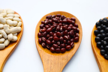 Three wooden spoons holding white, red, and black beans.