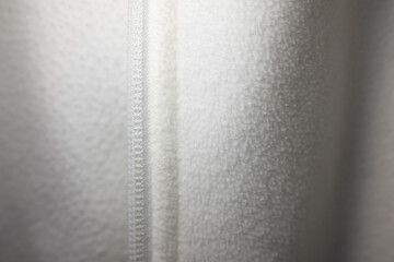 Macro shot of a white zipper on soft, light gray fleece fabric. The detailed texture and clean lines create a modern, sporty background with copy space. ©  Colorshadow