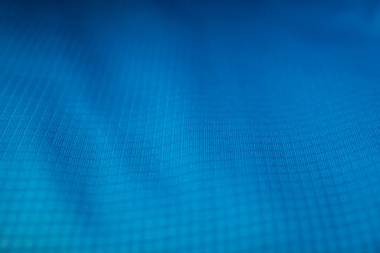 Macro detail of a vibrant blue technical fabric with a ripstop grid pattern. Ideal background for sportswear, outdoor gear, and technology themes.