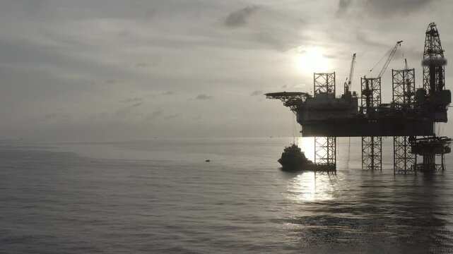 Aerial view from a drone of big jack up offshore drilling oil rig, production platform and supply vessel In the ocean during sunset - Oil and Gas Industry
