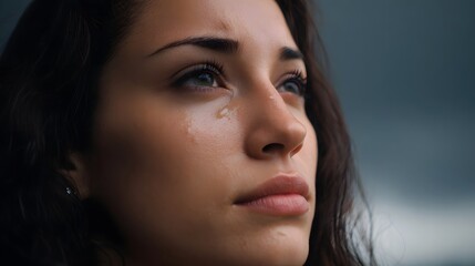 Fototapeta premium Close up portrait of a woman with tears looking up against a dramatic overcast sky