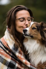 Young caucasian woman embracing dog outdoors in warm blanket
