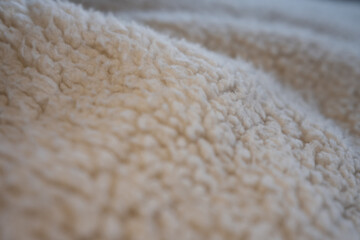 A macro shot of soft, cozy, cream-colored sherpa fleece fabric. The shallow depth of field creates a gentle, warm, and comfortable abstract background with soft folds.