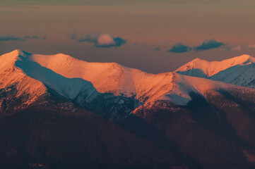 Aerial view of snow-capped peaks ablaze with the warm hues of sunset, painting the rugged landscape in shades of orange and blue, Derese, Zilina Region, Slovakia.