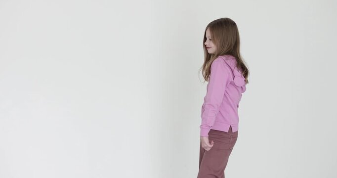 Girl in casual clothes walks across room with model-like stride on white background. Preteen child performs carefully measured model walk. Slow motion