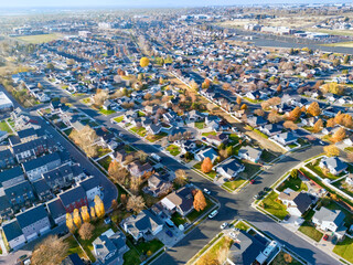 Aerial view of a suburban neighborhood with a mix of autumn colors on the trees and rooftops creates a warm and inviting scene, Layton, Utah, United States.