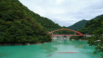 Kurobe Gorge valley featuring a red bridge spanning vibrant green water with a dam