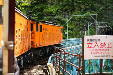 Orange train crossing a metal railway bridge next to a no trespassing sign