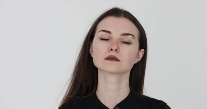 Serious woman with black long loose hair tilts head gently to stretch neck against white background. Female relieves tension in neck. Slow motion