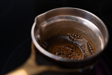Close-up of traditional Turkish coffee brewing in a cezve. The dark, rich foam bubbles up on a black stove, invoking a morning ritual.