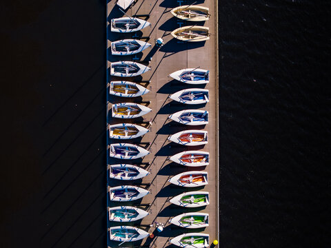Aerial view of a neat row of small boats with colorful interiors casting long shadows on a pier, contrasting with the dark water, Boston, Massachusetts, United States.