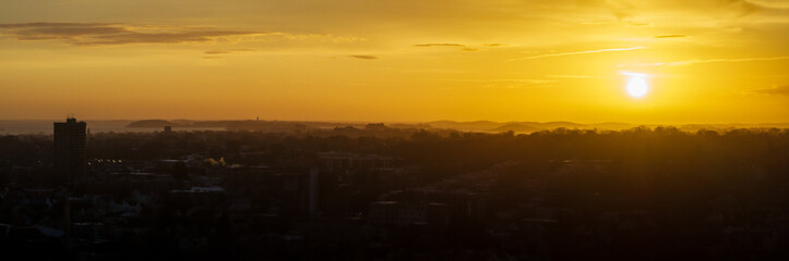 Aerial view of Boston's skyline silhouetted against a radiant sunrise, buildings and trees painted in hues of gold and umber, Boston, Massachusetts, United States.