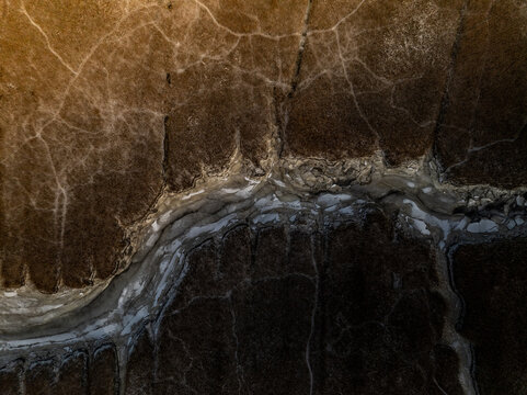Aerial view of a parched, cracked earth, the land split by a winding, silver stream reflecting the light, Boston, Massachusetts, United States.