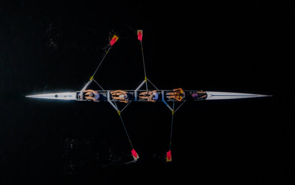 Aerial view of a sleek rowing boat slicing through the dark water, oars raised in unison, a testament to teamwork and precision, Boston, Massachusetts, United States.